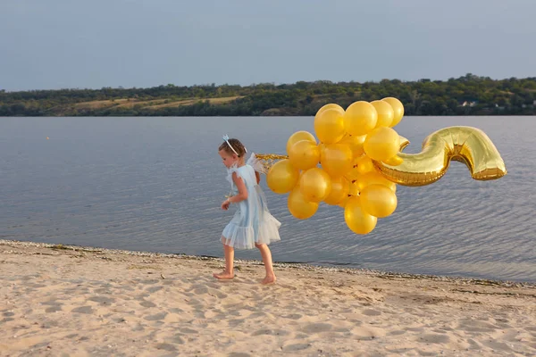 Niña con muchos globos dorados en la playa al atardecer — Foto de Stock