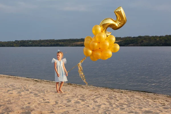 Gadis kecil dengan banyak balon emas di pantai saat matahari terbenam — Stok Foto