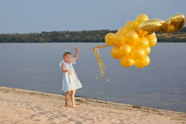 Menina com muitos balões dourados na praia ao pôr do sol — Fotografia de Stock