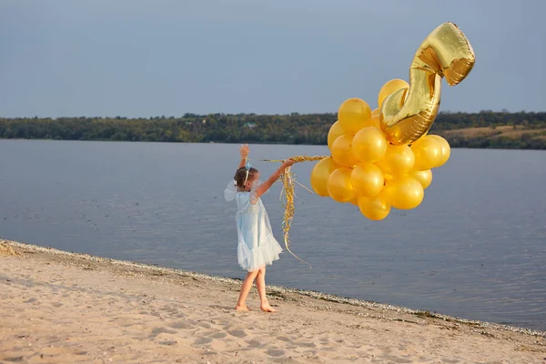 Liten flicka med många gyllene ballonger på stranden vid solnedgången — Stockfoto