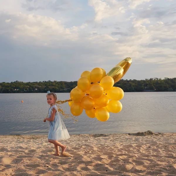 Bambina con tanti palloncini dorati sulla spiaggia al tramonto — Foto Stock