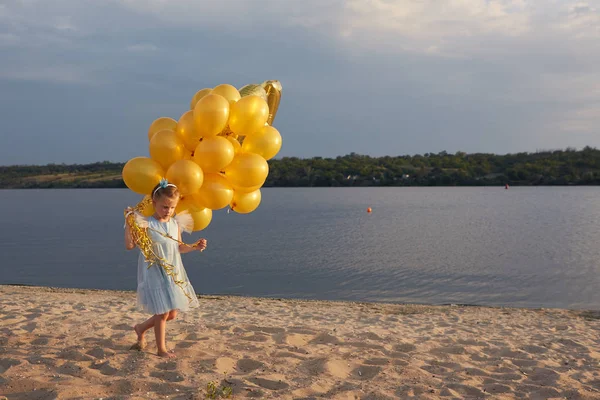 Menina com muitos balões dourados na praia ao pôr do sol — Fotografia de Stock