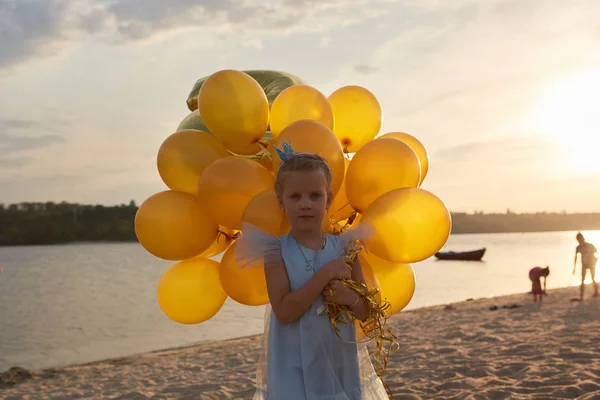夕暮れ時のビーチに多くの黄金風船持つ少女 — ストック写真