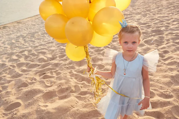 Liten flicka med många gyllene ballonger på stranden vid solnedgången — Stockfoto