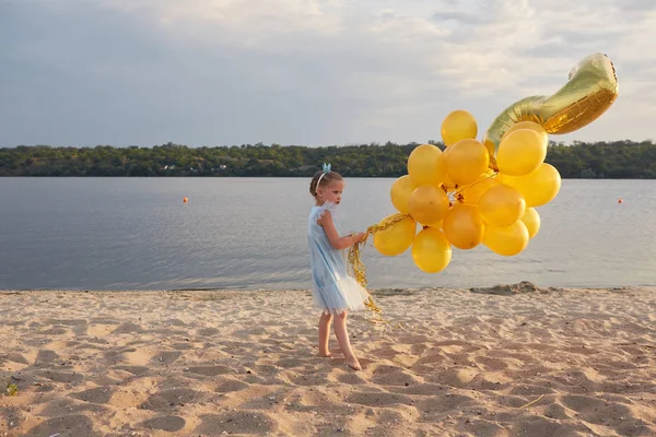 Dziewczynka z wielu złotych balony na plaży o zachodzie słońca — Zdjęcie stockowe