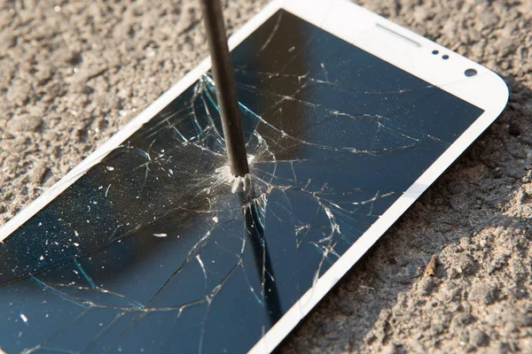 Clavo de metal y teléfono inteligente con una pantalla rota sobre la superficie de piedra. El concepto de fuerza . —  Fotos de Stock