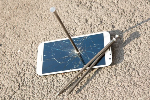 Metal nail and smartphone with a broken screen over the stone surface. The concept of strength. — Stock Photo, Image