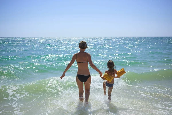 Zomer gelukkig gezin van zes jaar blond kind spelen en springen water golven omarmen vrouw moeder in zee strand — Stockfoto