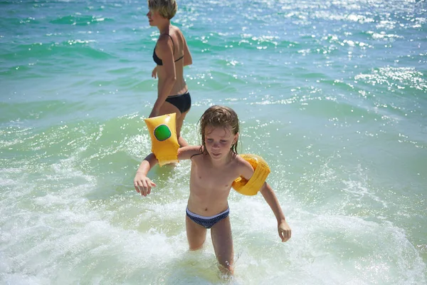Καλοκαίρι ευτυχισμένη οικογένεια έξι ετών ξανθό παιδί παίζει και άλματα κύματα νερού αγκαλιάζει τη γυναίκα μητέρα στη θάλασσα ακτή παραλία — Φωτογραφία Αρχείου