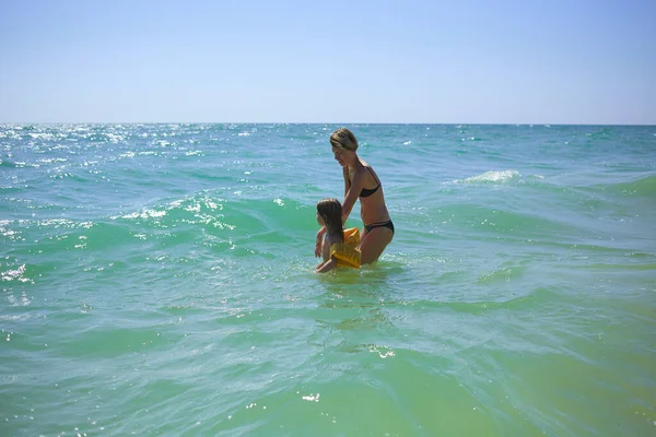 Sommer glückliche Familie von sechs Jahren blondes Kind spielt und springt Wasserwellen umarmt Frau Mutter in Strand am Meer — Stockfoto