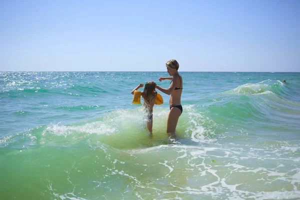 Zomer gelukkig gezin van zes jaar blond kind spelen en springen water golven omarmen vrouw moeder in zee strand — Stockfoto