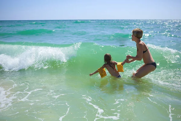 Verão feliz família de seis anos de criança loira brincando e pulando ondas de água abraçando mulher mãe na praia do mar — Fotografia de Stock