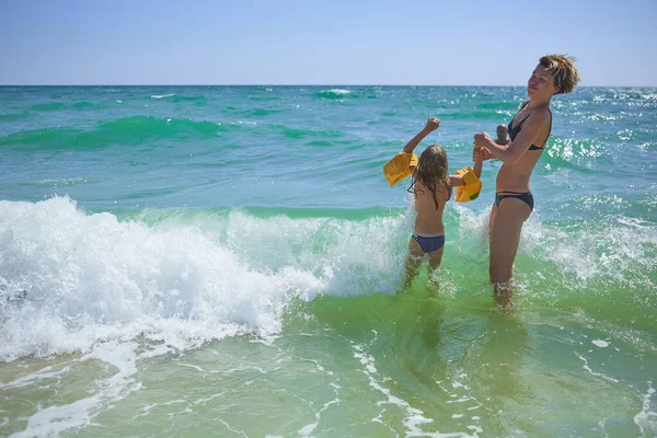 Zomer gelukkig gezin van zes jaar blond kind spelen en springen water golven omarmen vrouw moeder in zee strand — Stockfoto