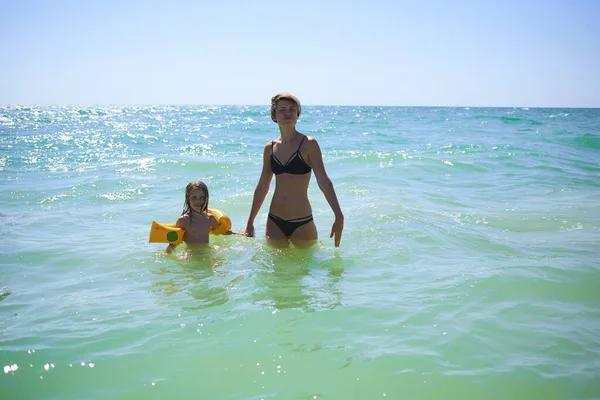 夏天快乐的家庭，有6岁的金发碧眼的孩子，在海滨海滩玩耍，跳跃着海浪拥抱着妈妈 — 图库照片