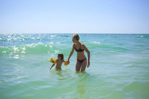 Verano feliz familia de seis años niño rubio jugando y saltando olas de agua abrazando a la mujer madre en la playa de la orilla del mar — Foto de Stock