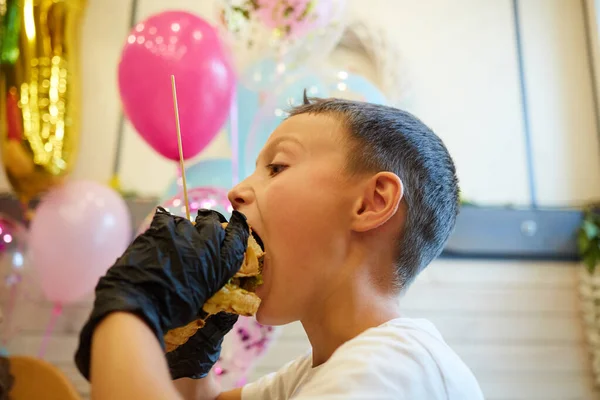 The handsome little boy eating burger in black rubber gloves. — Stock Photo, Image