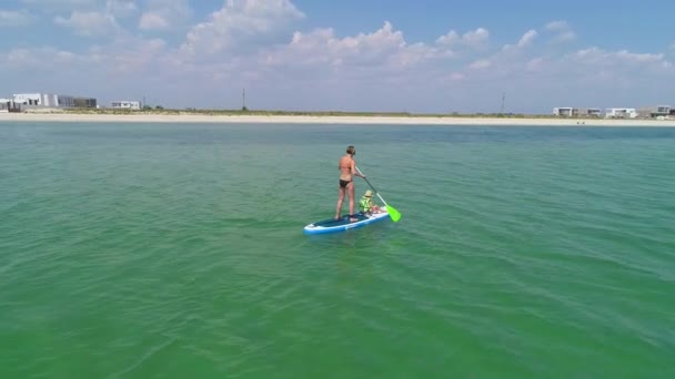 Kleines Mädchen in Schwimmweste sitzt mit Mutter auf dem Paddelbrett. — Stockvideo