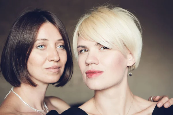 Portrait of two attractive caucasian smiling women blonde and brunette studio shot short hair looking at camera. — Stockfoto