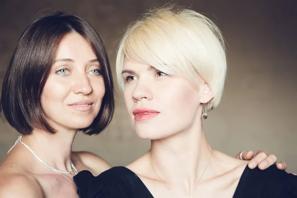 Portrait of two attractive caucasian smiling women blonde and brunette studio shot short hair looking at camera. — Stockfoto