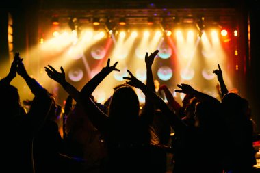 Parlak sahne ışıkları önünde konser kalabalığının siluetleri