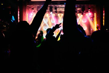 Parlak sahne ışıkları önünde konser kalabalığının siluetleri