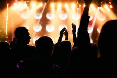 Parlak sahne ışıkları önünde konser kalabalığının siluetleri