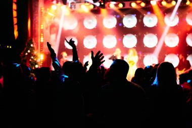 Parlak sahne ışıkları önünde konser kalabalığının siluetleri