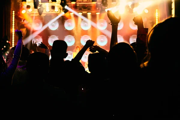 Crowd at a music concert, audience raising hands up in front of bright stage lights. — Stock Photo, Image