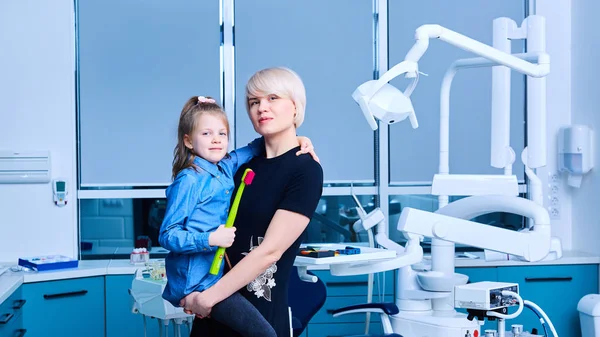 Moeder en haar daugter op de achtergrond tandheelkundige kliniek interieur met stoel en gereedschap. — Stockfoto