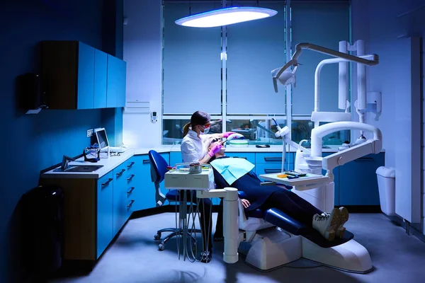 Žena Zubař velmi pečlivě zkontrolovat a opravit zub své mladé pacientky. Šťastná mladá žena sedí v zubním křesle u zubaře kancelář — Stock fotografie
