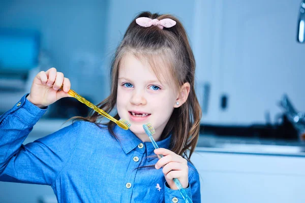 Una niña linda cepillándose los dientes con dos cepillos de dientes . — Foto de Stock