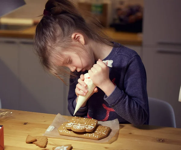 Glad liten flicka dekorera en hemmagjord pepparkakor med glasyr på träbord. — Stockfoto