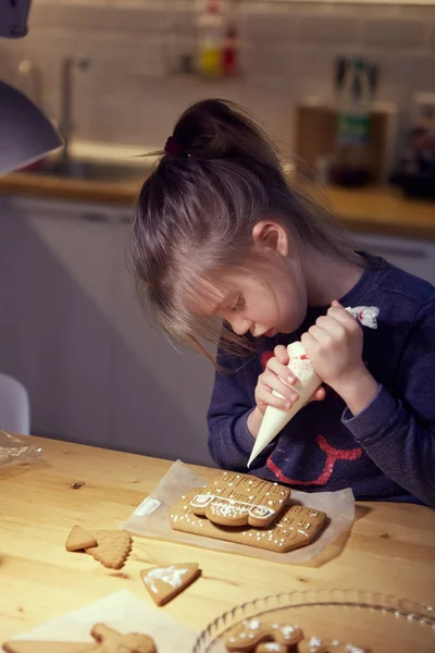 나무 식탁에서 유약을 사용하여 집에서 진저브레드 쿠키를 꾸미고 있는 행복 한 소녀. — 스톡 사진