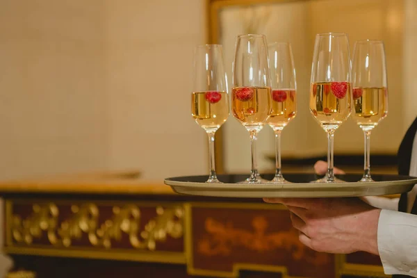 Ober serveert Champagne met aardbeien op een dienblad. — Stockfoto