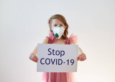 7 yaşında, tıbbi maskeli bir kız üzerinde Stop COVID-19 mesajı olan bir poster tutuyor. Konsept 2019-NCov. Corona virüsü salgını. Salgın Virüs Solunum Sendromu. 2019 Coronavirus bayrağı