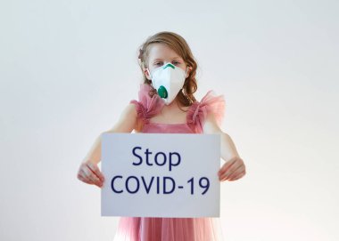 7 yaşında, tıbbi maskeli bir kız üzerinde Stop COVID-19 mesajı olan bir poster tutuyor. Konsept 2019-NCov. Corona virüsü salgını. Salgın Virüs Solunum Sendromu. 2019 Coronavirus bayrağı