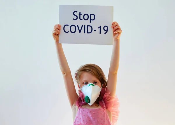 7-letnia dziewczynka w masce medycznej trzyma plakat z wiadomością Stop COVID-19. Koncepcja 2019-nCov. Epidemia wirusa korony. Zespół oddechowy wirusa epidemii. Sztandar koronawiru na 2019 r. — Zdjęcie stockowe