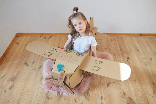 Pequeña chica soñadora jugando con un avión de cartón. Infancia. Fantasía, imaginación . — Foto de Stock