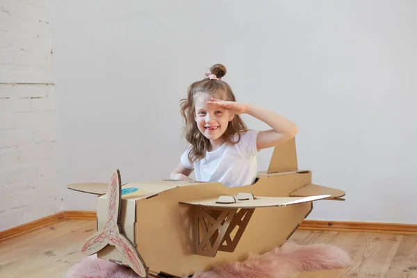 Pequeña chica soñadora jugando con un avión de cartón. Infancia. Fantasía, imaginación . — Foto de Stock