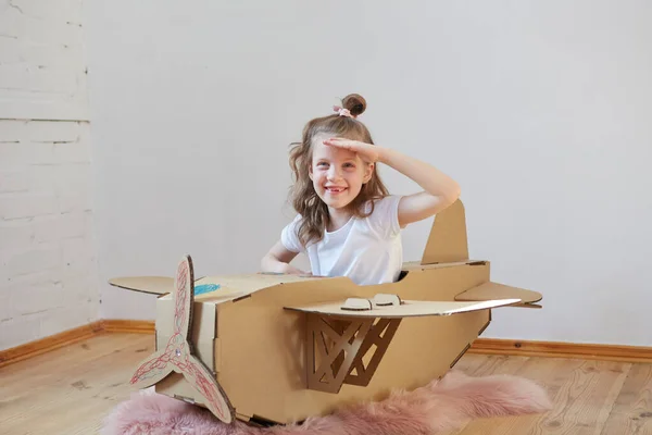 Pequeña chica soñadora jugando con un avión de cartón. Infancia. Fantasía, imaginación . — Foto de Stock