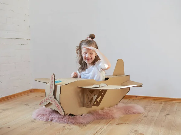 Pequeña chica soñadora jugando con un avión de cartón. Infancia. Fantasía, imaginación . — Foto de Stock