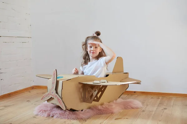 Pequeña chica soñadora jugando con un avión de cartón. Infancia. Fantasía, imaginación . —  Fotos de Stock