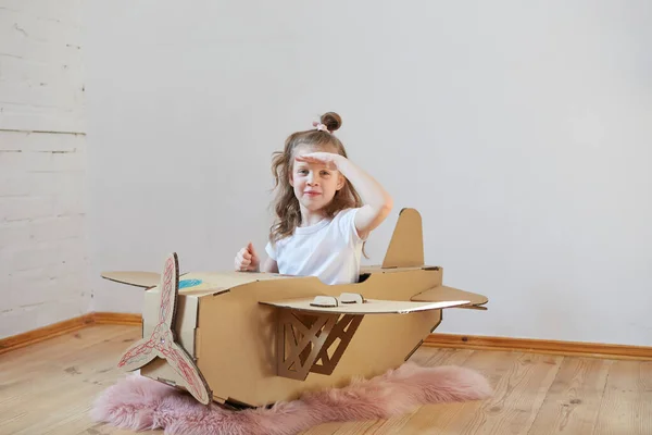 Pequeña chica soñadora jugando con un avión de cartón. Infancia. Fantasía, imaginación . — Foto de Stock