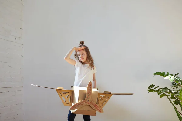 Pequeña chica soñadora jugando con un avión de cartón. Infancia. Fantasía, imaginación . — Foto de Stock