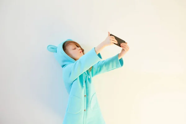 Vrolijk klein meisje 7 jaar oud maken een selfie op de witte achtergrond. Concept Sociale Media Verslaving. — Stockfoto