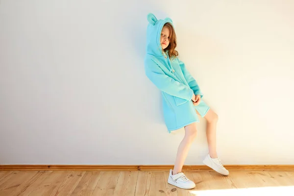 Jolie fille de sept ans se tient près d'un mur blanc et souriant. Mode pour enfants. Style printemps . — Photo