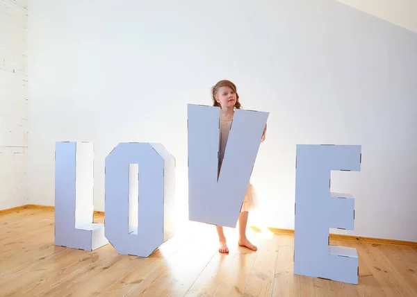 7-jähriges Mädchen beim Spielen mit großen 3D-Buchstaben aus Pappe, die auf hellem Hintergrund das Wort LIEBE bilden. Beziehungskonzept. — Stockfoto