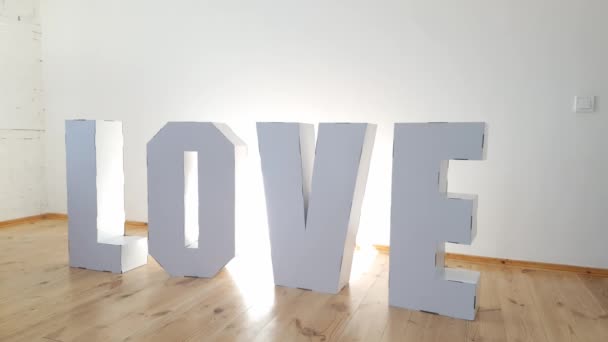 Dívka 7 let hraje s velkou lepenkou 3D stojící písmena tvořící slovo LOVE z bílého kartonu na světlém pozadí. Koncept vztahu. — Stock video