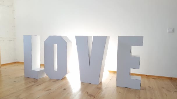 7 yaşında bir kız, arka planda beyaz kartondan "Aşk" kelimesini oluşturan üç boyutlu büyük karton harflerle oynuyor. İlişki kavramı. — Stok video
