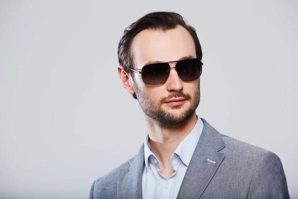 Elegante joven guapo hombre en gafas de sol y en chaqueta gris con estilo. Estudio retrato de moda . — Foto de Stock